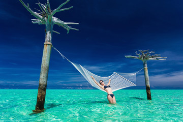 Woman relaxing on over-water hammock in the middle of tropical l