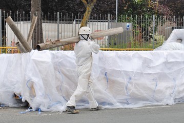 Trabajador de amianto lleva una tuberia de fibrocemento al saco para meter amianto que está dentro del contenedor