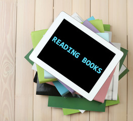 PC tablet on  top of pile of books and magazines on wooden background