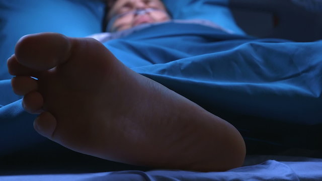 Doctor giving electric shocks with defibrillator to dying man who lies in a hospital bed to try to revive him.