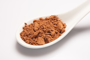 Pile of cacao powder in white ceramic spoon