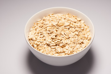 Raw oatmeal flakes in white ceramic bowl on white background