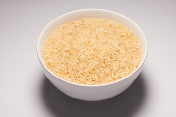 Brown rice seeds in white ceramic bowl on white background