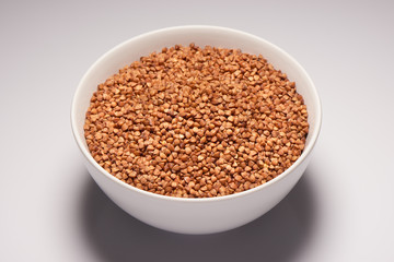 Buckwheat seeds in white ceramic bowl on white background