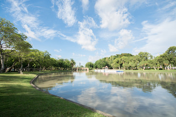 View of park with lake, blue sky, clouds and green leaves of tre