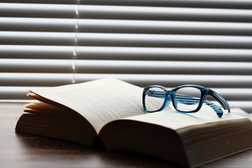 Book glasses.
Pair of glasses on a book with blind in the background.