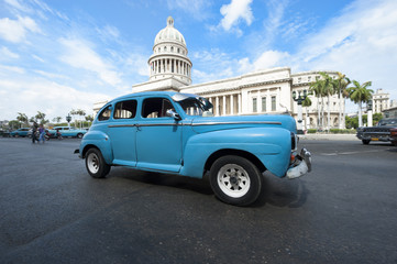 Classic blue American car passes in front of the Capitolio building in Central Havana