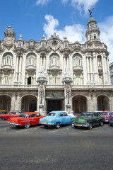 Row of brightly colored vintage American cars stand parked in front of eye-catching colonial architecture