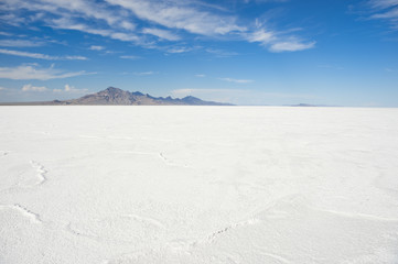 Dramatic white desert background of textured salt formations with rugged mountain range on the horizon