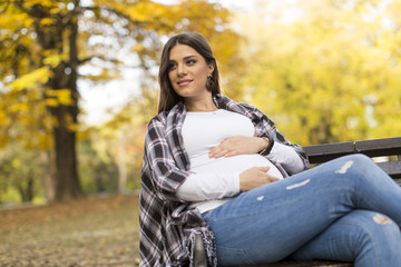Fototapeta na wymiar Young pregnant woman sitting in the autumn park