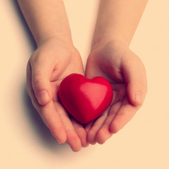 Heart in child hands on light background