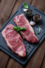 Basalt dish with two fresh striploin steaks and seasonings