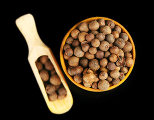 Allspice in wooden bowl, isolated on black