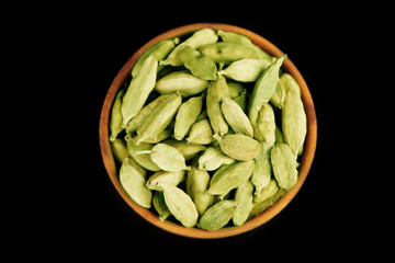 Cardamom in wooden bowl, on black background