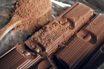 Bar of chocolate with cocoa on foil, closeup