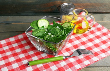 Glass bowl of green salad with cucumber and spinach on wooden table with napkin, closeup