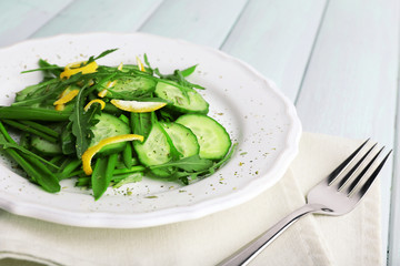 Green salad with cucumber, arugula and lemon peel on wooden background