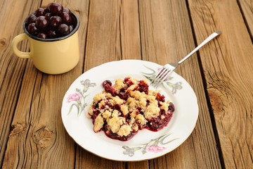 Piece of delicious homemade cherry crumble with fork in white pl