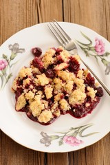 Piece of homemade juicy cherry crumble with fork in white plate
