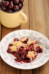 Piece of homemade cherry crumble with fork and yellow metal cup