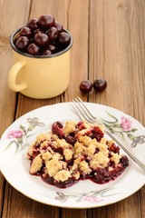 Piece of homemade cherry crumble with fork and yellow metal cup