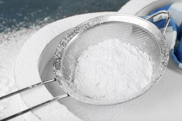 Sifting flour through sieve on wooden table, closeup