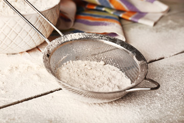 Sifting flour through sieve on wooden table, closeup
