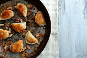 Fried dumplings with onion and bacon in frying pan, on wooden table background