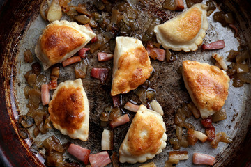 Fried dumplings with onion and bacon in frying pan
