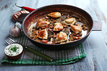 Fried dumplings with onion and bacon in frying pan, on wooden table background