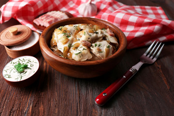 Fried dumplings with onion and bacon in frying pan, on wooden table background