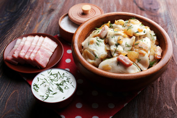 Fried dumplings with onion and bacon in frying pan, on wooden table background
