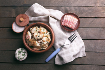 Fried dumplings with onion and bacon in frying pan, on wooden table background