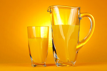 Glass and pitcher of orange juice on orange background