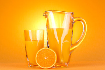 Glass and pitcher of orange juice on orange background