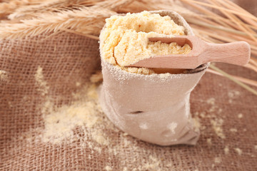Flour in bag with wheat ears and wooden scoop on burlap cloth, closeup