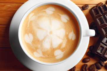 Cup of coffee latte art with grains and chocolate bar on wooden table, closeup