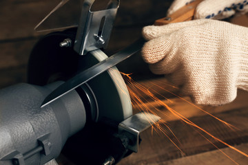 Knife sharpener and hand with blade on wooden table, closeup