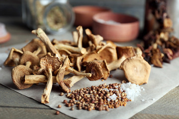 Dried mushrooms with spices on paper on wooden table, closeup