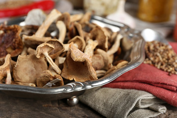 Dried mushrooms in metal tray with spices on wooden table, closeup