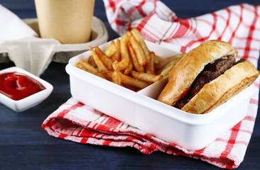 Tasty burger and french fries on plate, on wooden table background. Unhealthy food concept