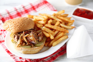 Tasty burger and french fries on plate, on wooden table background. Unhealthy food concept