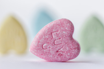 horizontal close up image of a little pink heart candy that says Love You with three candy hearts blurred in background isolated on white with room for text.