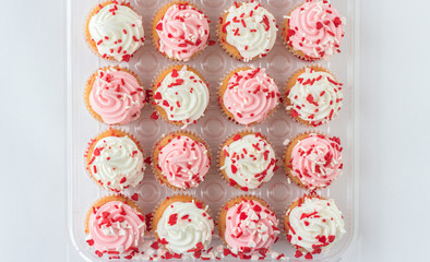 horizontal image of a group of muffins with white and pink icing with little red valentine candy sprinkles isolated on white background with room for text.