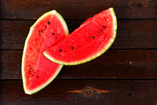 Two slices of watermelon on dark wet wooden table seen from above