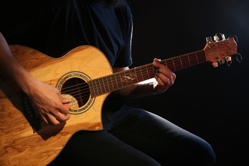 Naklejka na ściany i meble Young man playing on acoustic guitar on dark background