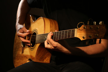 Obraz premium Young man playing on acoustic guitar on dark background