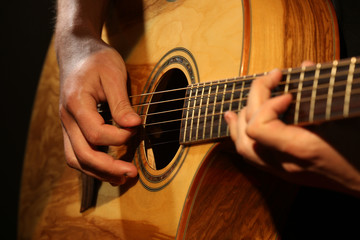 Young man playing on acoustic guitar close up