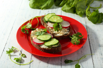 Delicious sandwiches with vegetables and greens on plate on table close up