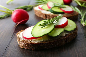 Delicious sandwiches with vegetables and greens on wooden table